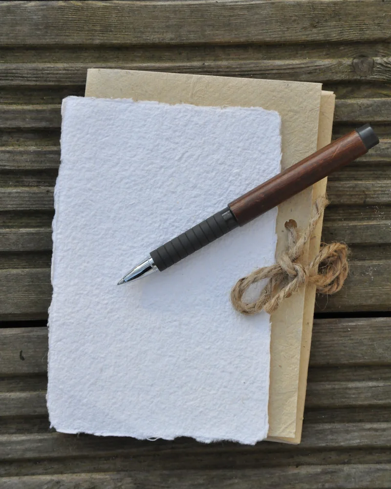 A pen and handmade paper stationery on a weathered wood table